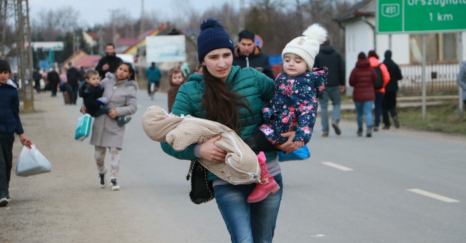 A young Ukrainian mother carries her three-month-old baby and her three-year-old toddler across the Tiszabecs border crossing into Hungary after she fled Ukraine leaving her husband behind. On arrival, Ukrainians and other nationalities are screened and registered. They are guided to assembly points where they can apply for asylum and are given temporary documentation. ; Russia launched its military offensive in Ukraine on 24 February 2022. By 27 February, hundreds of thousands of people had fled to safety inside Ukraine or neighbouring countries. The largest numbers headed west into Poland, with others making for Hungary, Moldova, Romania and beyond.